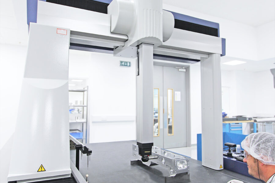 Man in laboratory clothing operating a Mitutoyo CMM using a handheld controller.